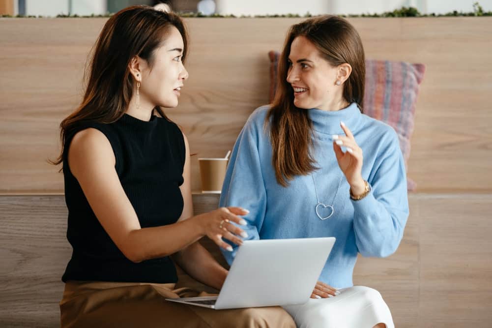 two woman talking to each other with a laptop illustrating guide to website localization for business owners